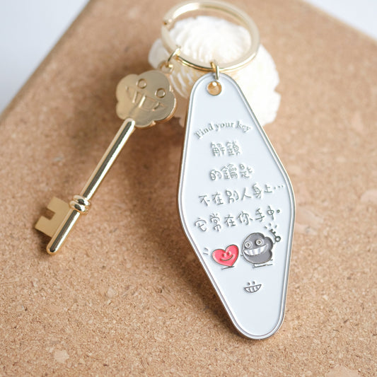 A metal keychain with a rectangular tag featuring Chinese characters, a small heart, and a dust mite design, attached to a gold-colored key.