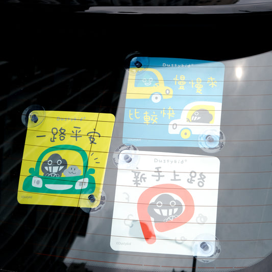 Three colorful car stickers with cartoon designs and text on a car window.
