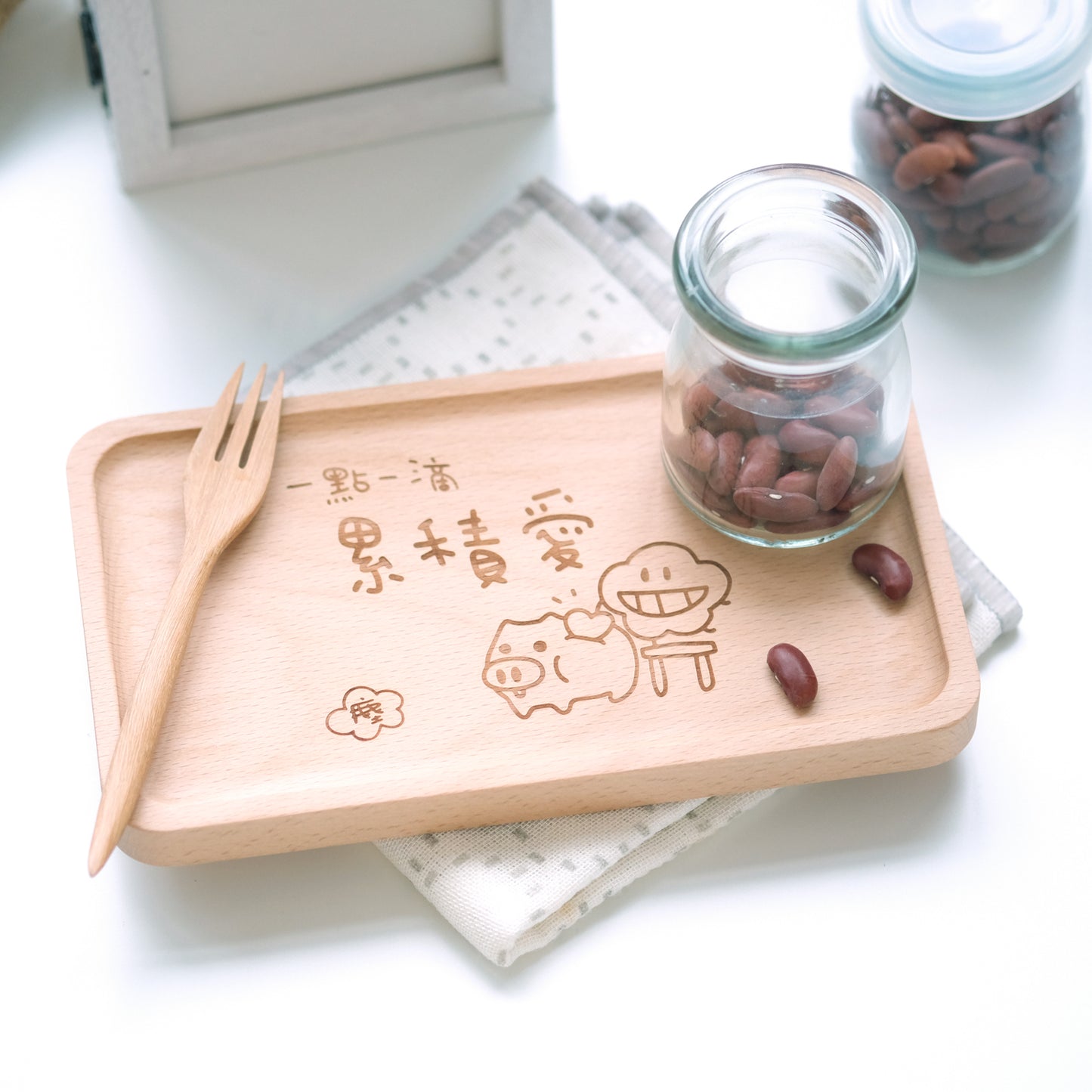 Wooden tray with engraved designs, glass jar, and wooden sticks on a white surface.