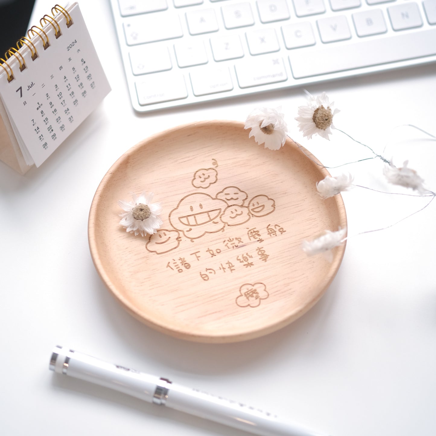 Wooden plate with engraved design on a white desk with keyboard and pen